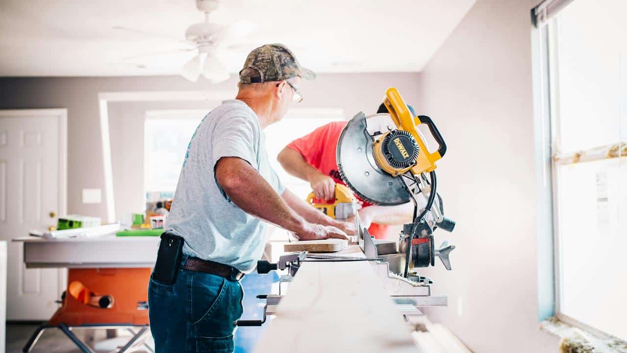 An older man using a miter saw indoors.