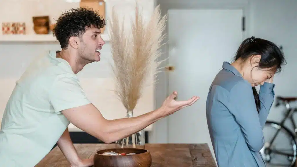 A man gestures with an open hand toward a woman who is looking down and away.