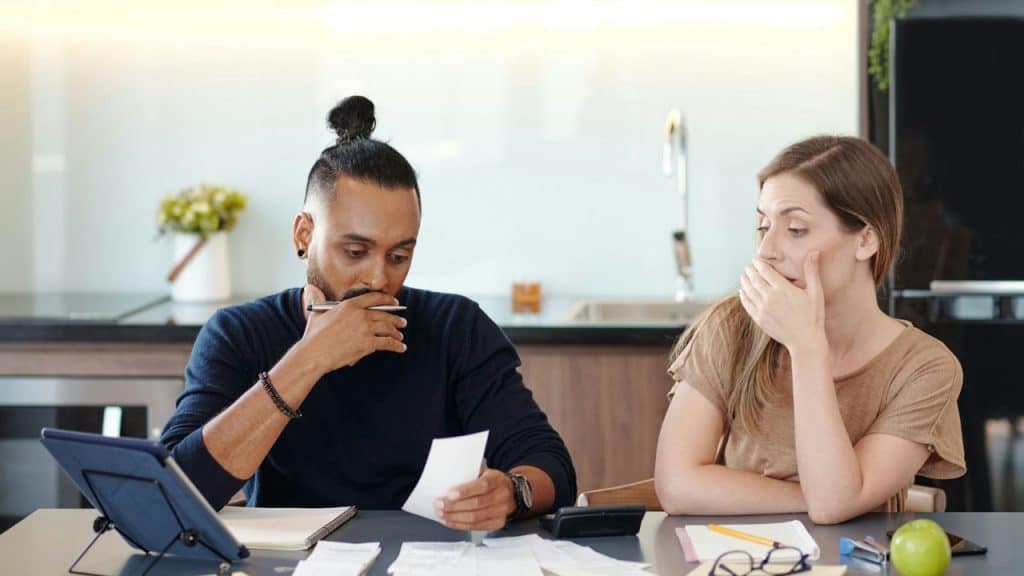 A man looks at a paper while a woman sits next to him covering her mouth.