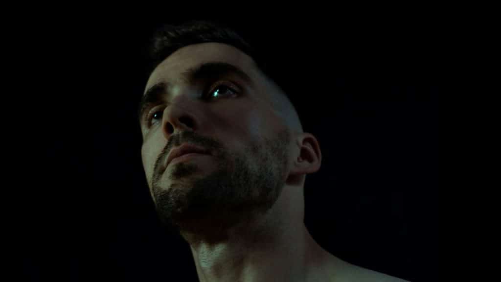A close-up view of a bearded man's face looking upward against a dark background.