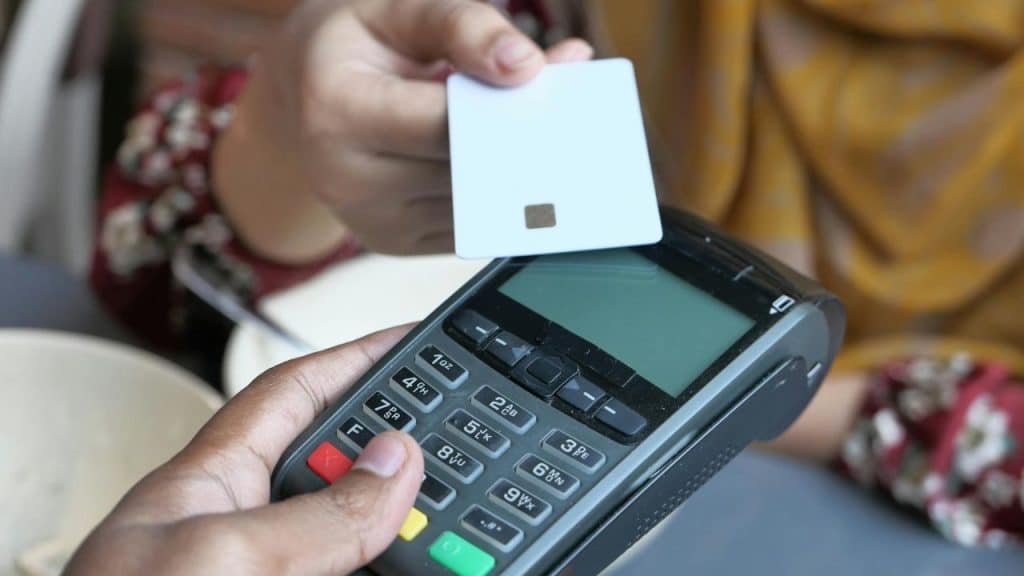 Close-up of a hand holding a white card over an electronic handheld payment terminal.