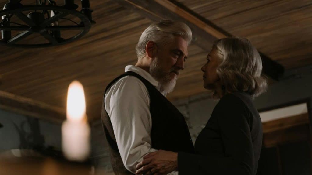 An older man with a white beard and an older woman look at each other closely.