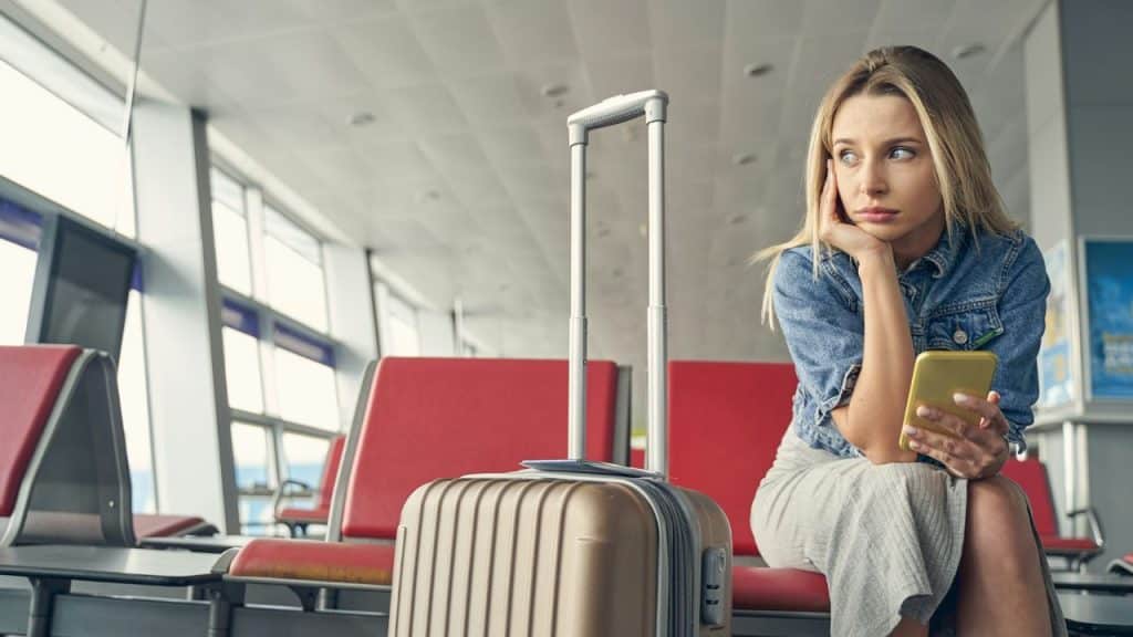 A woman sits in an airport terminal holding a phone and resting her chin.