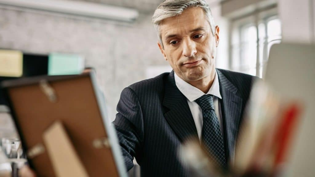 A man in a pinstripe suit looks down sadly at a framed picture on a desk.