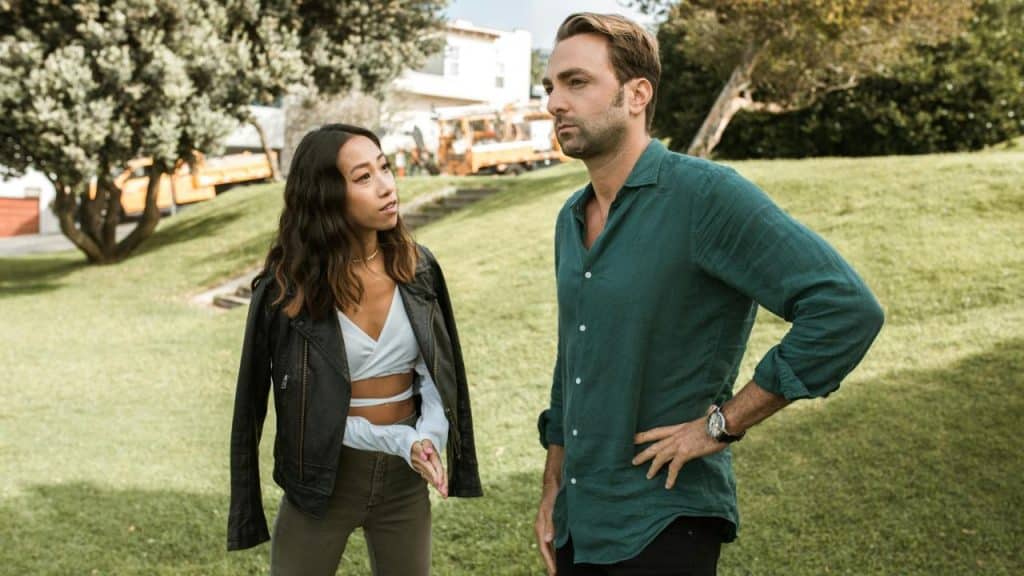 A woman in a leather jacket talks to a man in a green shirt outdoors.