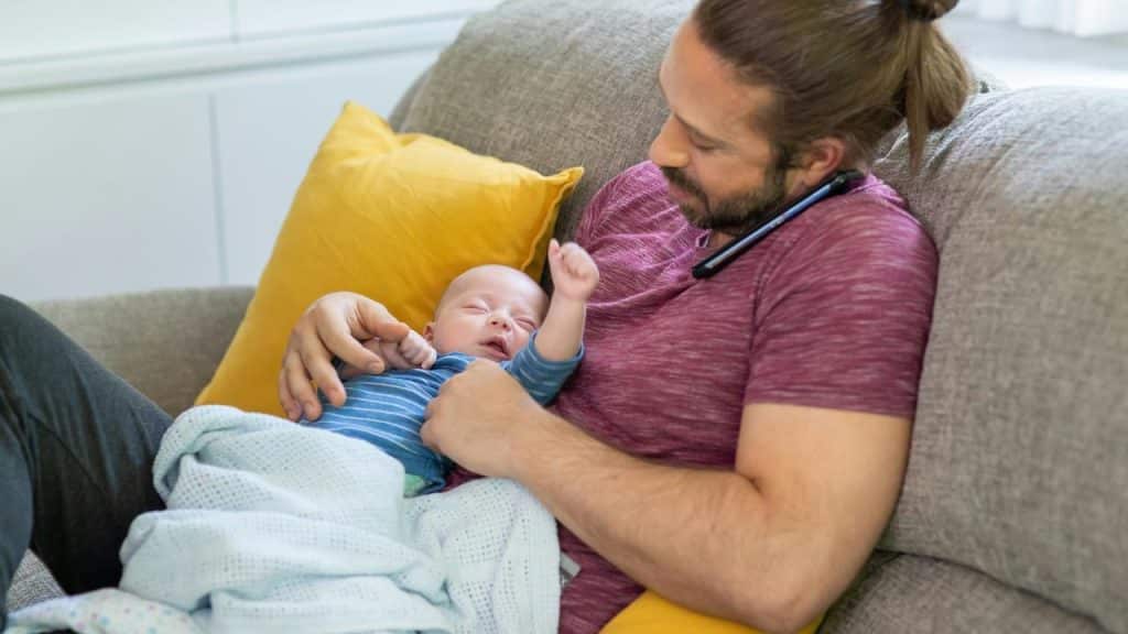 A man relaxing on a couch while holding a baby in his arms.