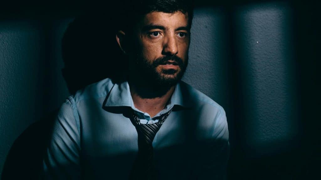 A man in a dimly lit room wearing a loosened tie and looking serious.