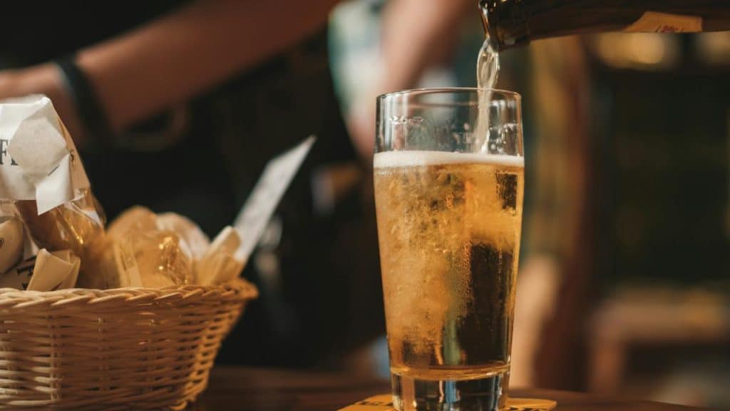 A glass of beer being poured on a table beside a basket of snacks.