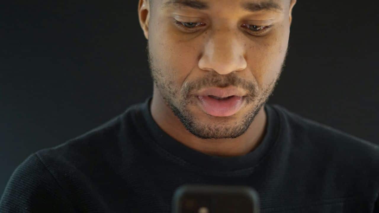 A close-up shot of a man looking down at his smartphone with a neutral expression.