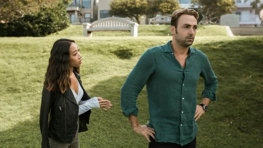 A man in a green shirt stands with hands on hips while a woman talks to him.