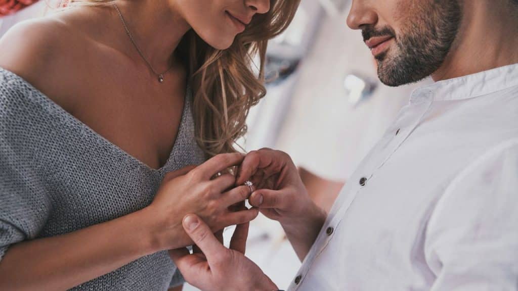 Close-up of a man placing a diamond ring onto the finger of a woman's left hand.