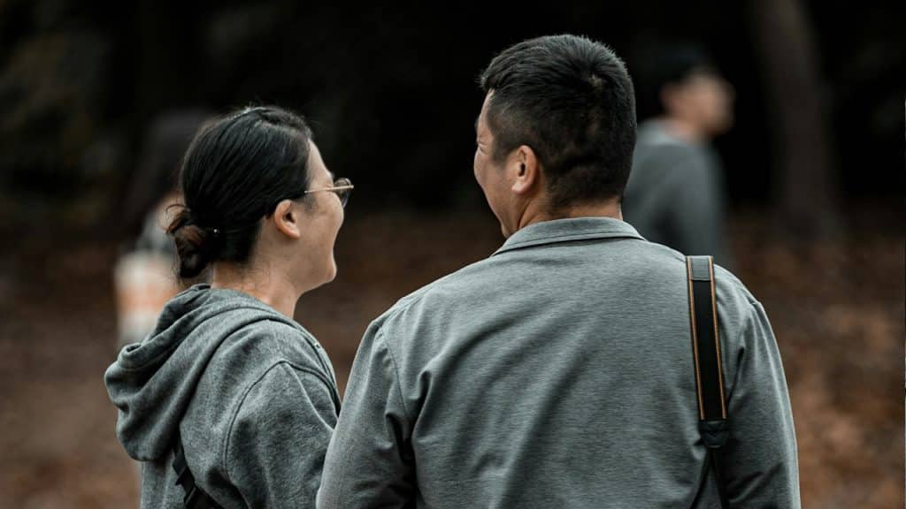 A couple standing with their backs to the camera and smiling at each other.