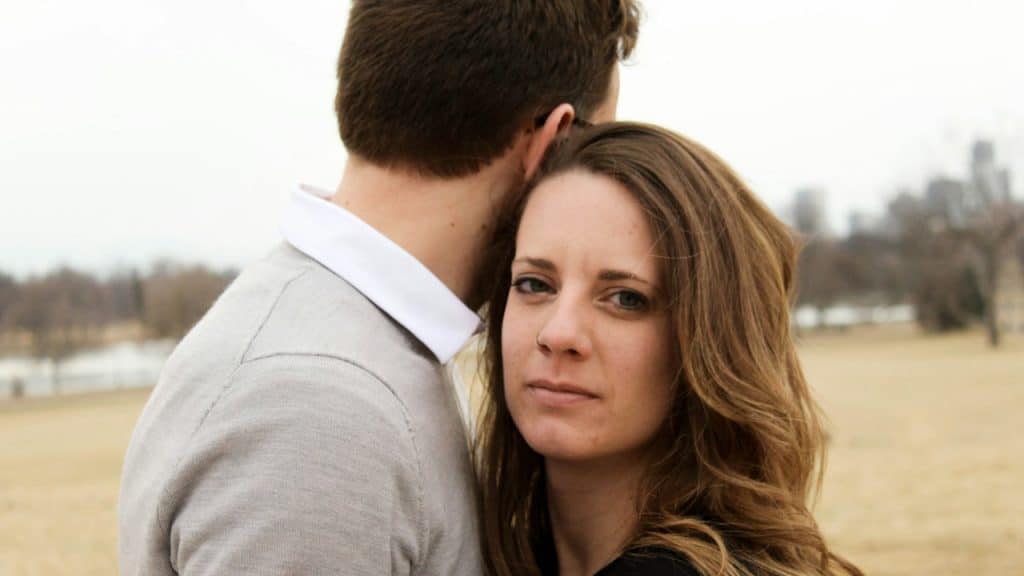 A man in a grey and white collared shirt and a woman in black top are standing close to each other.