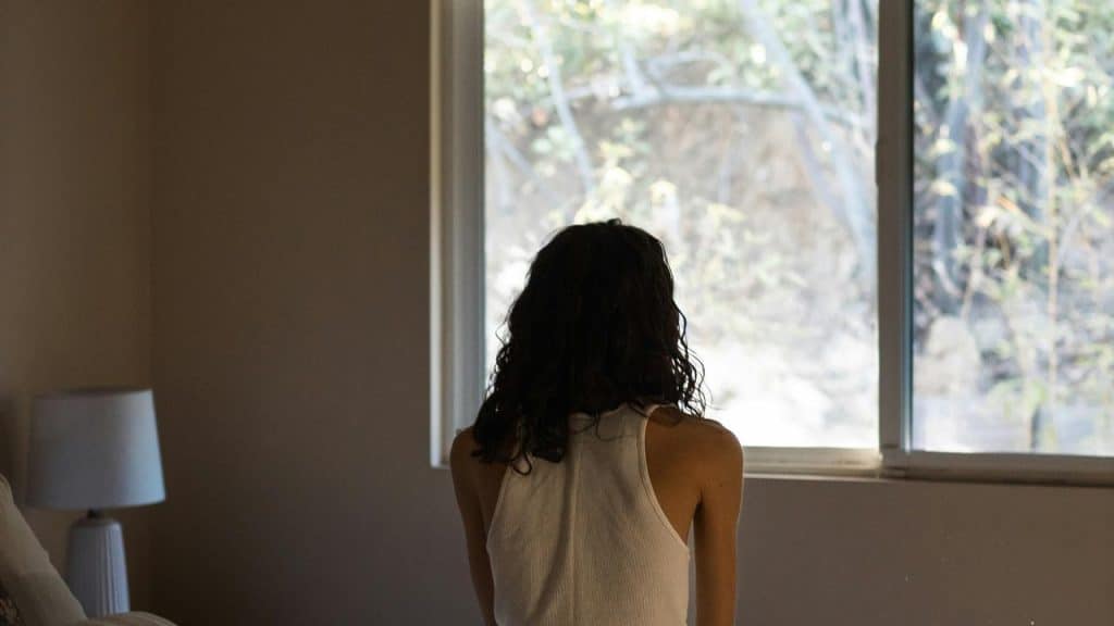 A person standing indoors and looking out a window.