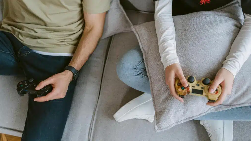 A close-up of two people sitting on a couch, each holding a video game controller.