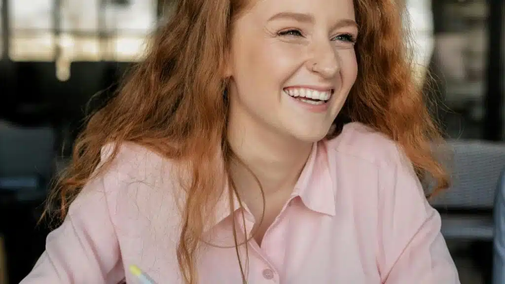 A woman with long red hair smiles while sitting at a table.