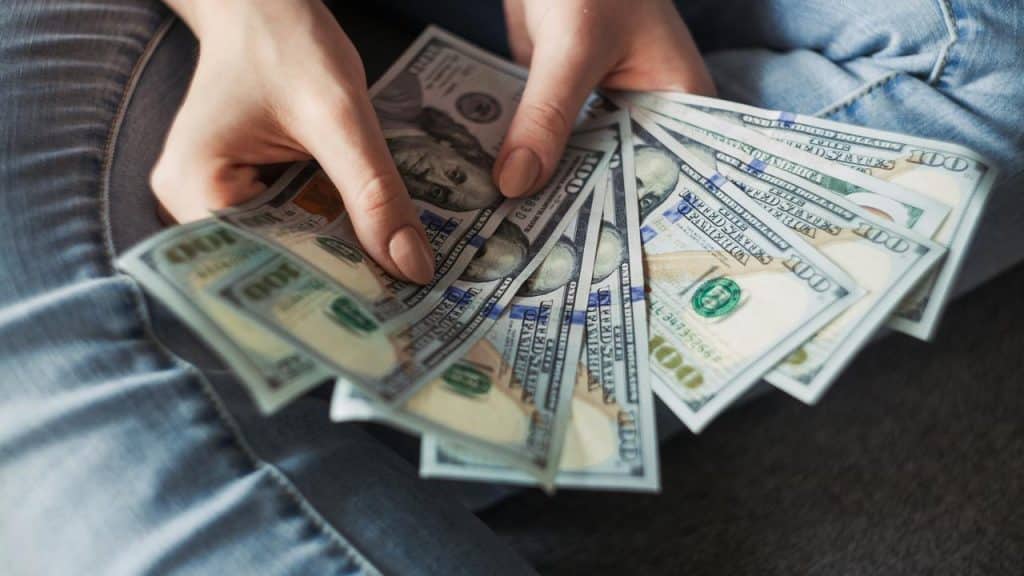 A person holding a fan of US hundred-dollar bills.