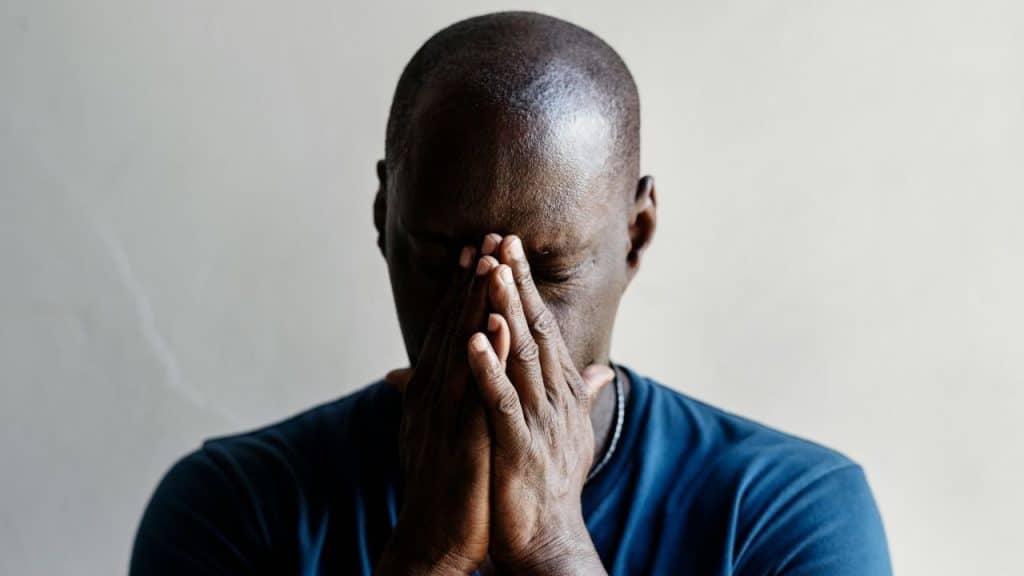 A person in a blue shirt holds their face in their hands with eyes closed.