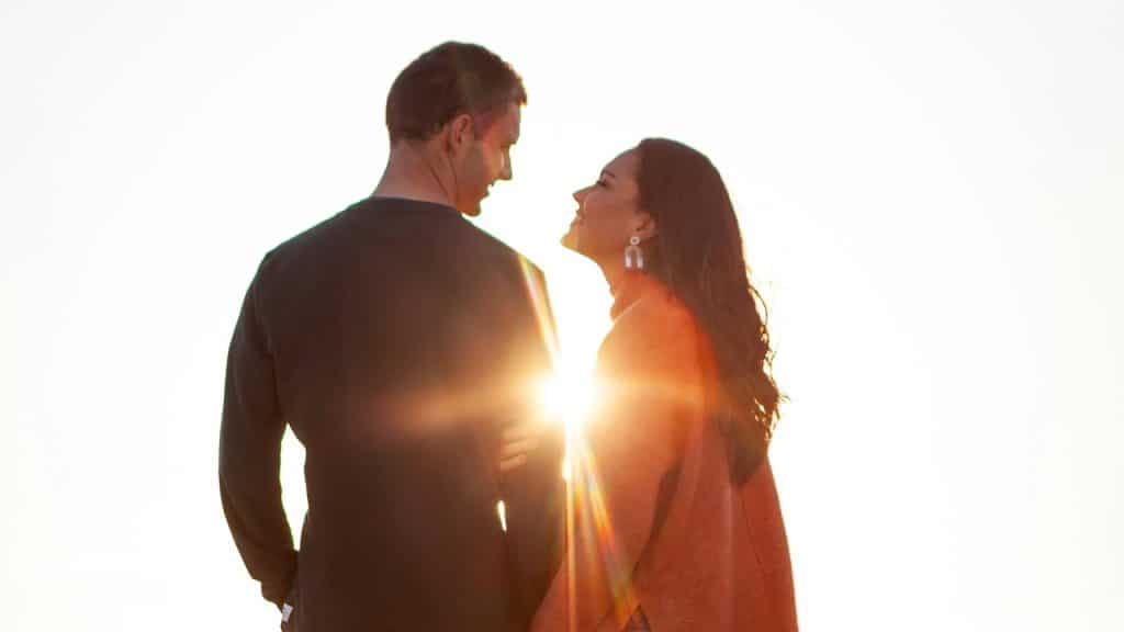 A woman gazing into a man’s eyes while they stand in front of the sun.