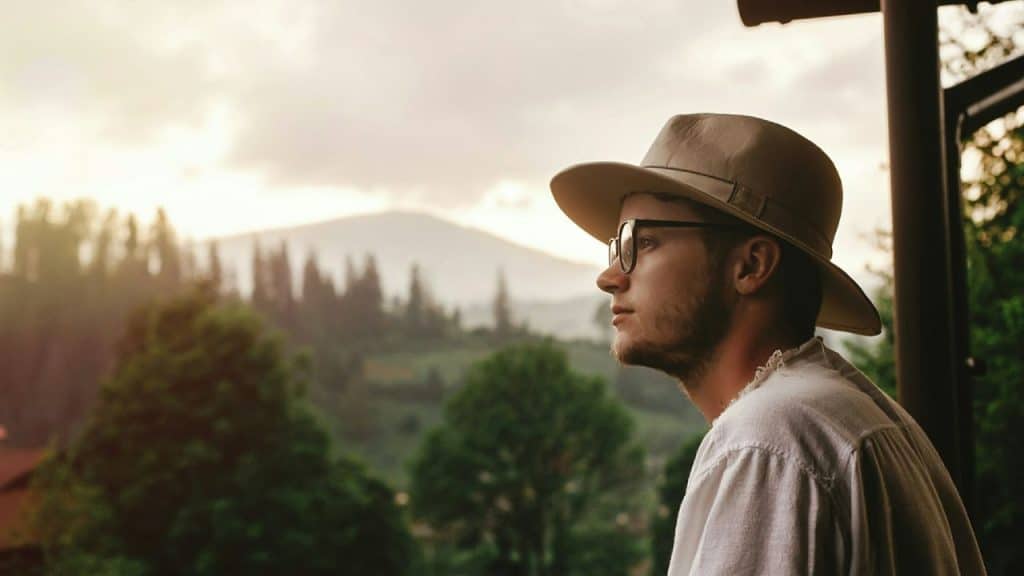 Side profile of a man wearing a hat and glasses looking out at a landscape.