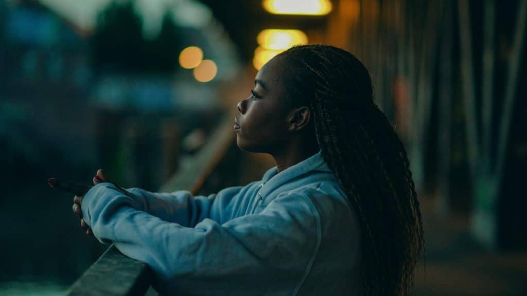 A woman leaning on a railing at night, gazing into the distance under soft streetlights.