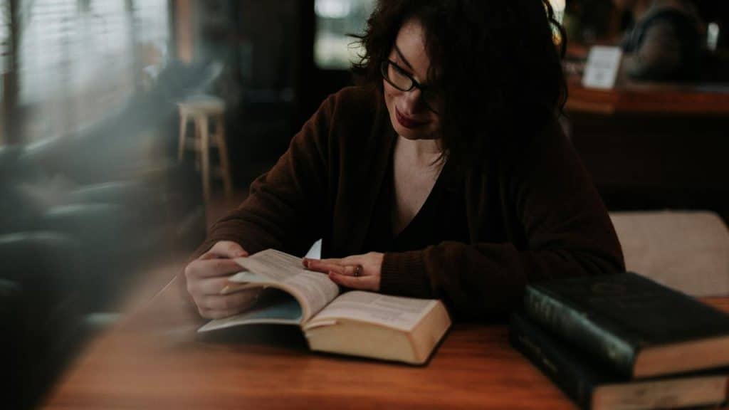 A woman reading a book at a wooden table indoors.