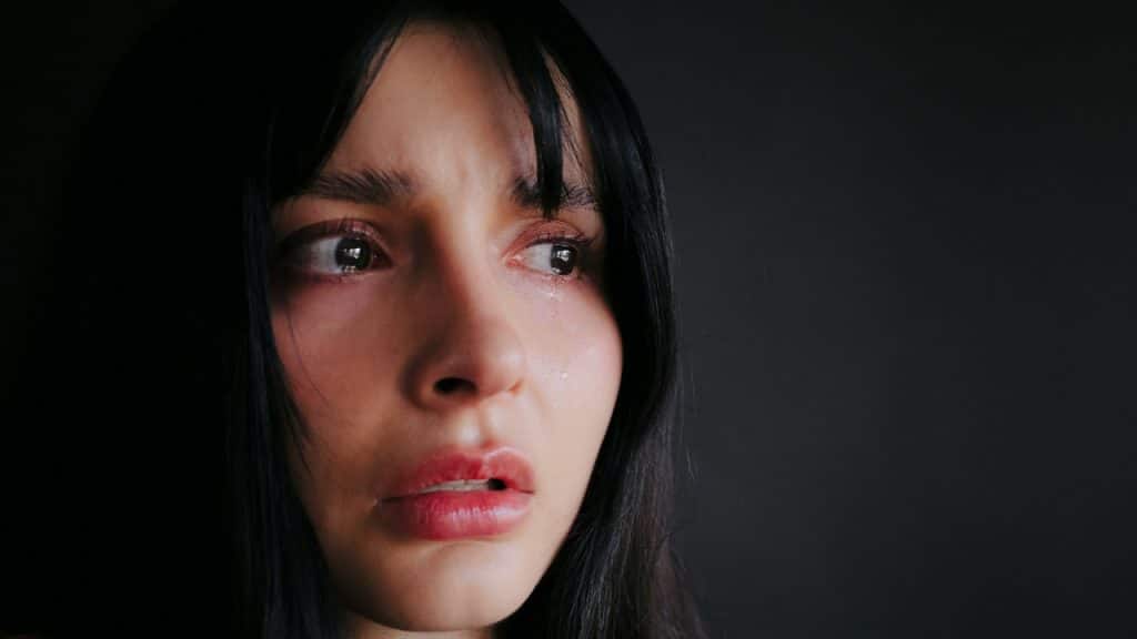 Close-up of a person with dark hair, wide eyes, and a single tear on their cheek.