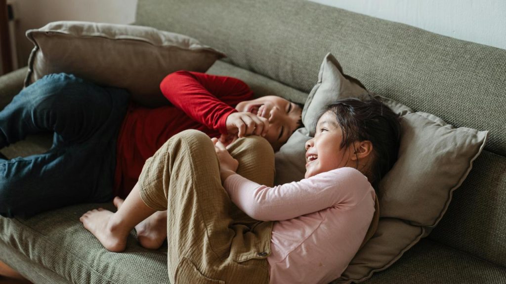 A boy and girl laughing together on a couch.