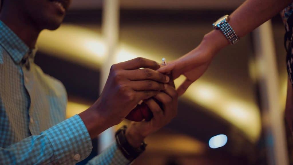 A person placing an engagement ring on another person’s finger.
