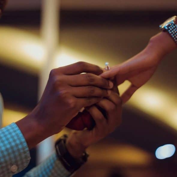 A person placing an engagement ring on another person’s finger.