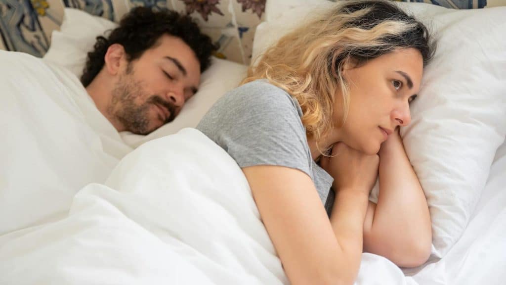 A woman lying on the bed beside a sleeping man.