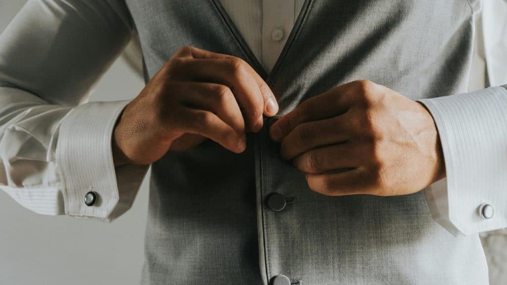 A man buttoning a grey vest over a white dress shirt.