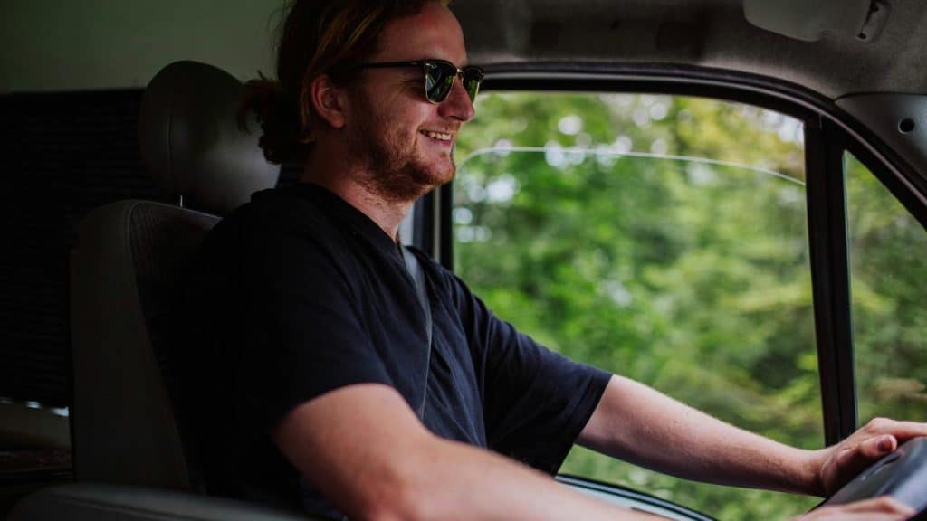 A smiling person wearing sunglasses while driving a vehicle.