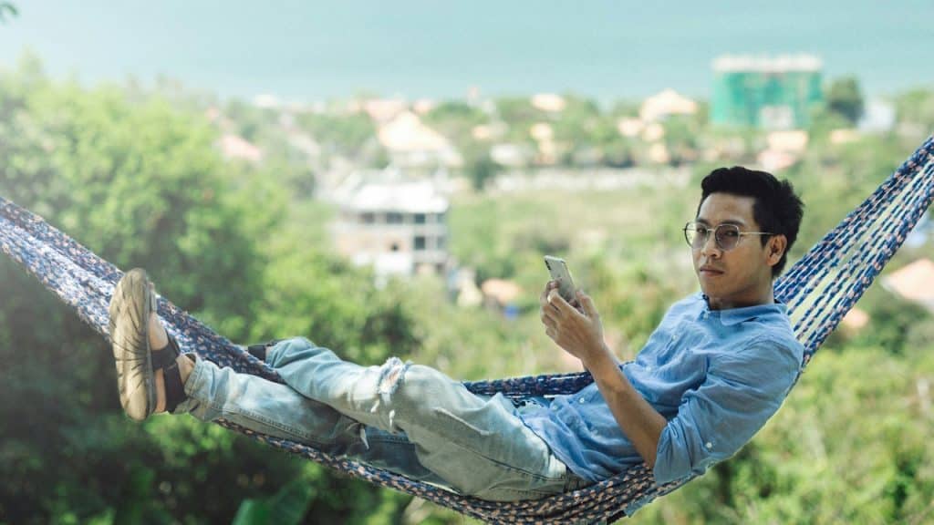 A man in a blue polo shirt sitting on a white metal fence during the daytime.