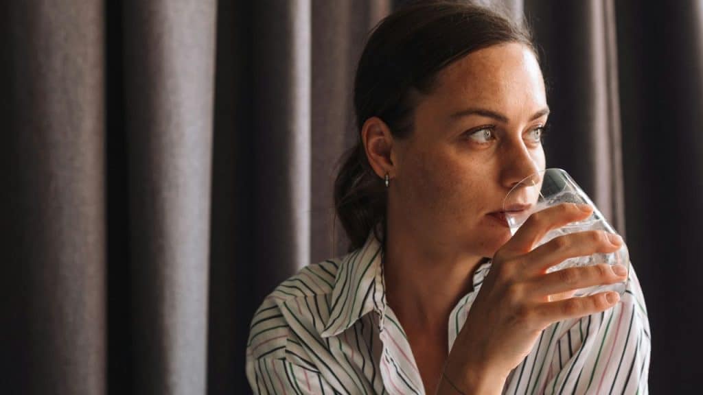 A woman in a striped shirt drinks from a glass, looking to her right.