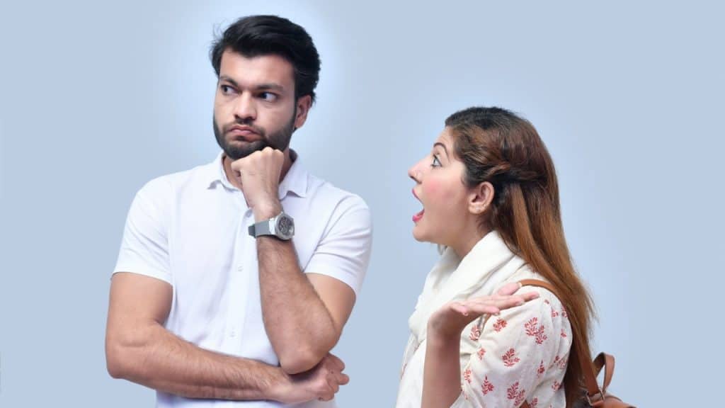 A woman with her mouth open and hand raised gestures toward a man looking away.