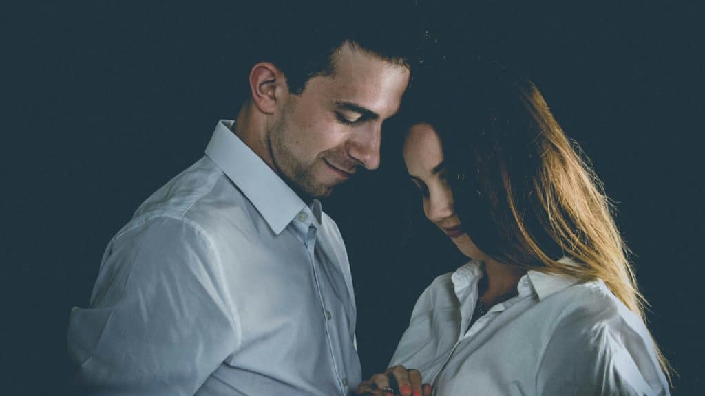 A smiling couple standing close to each other and looking downwards.