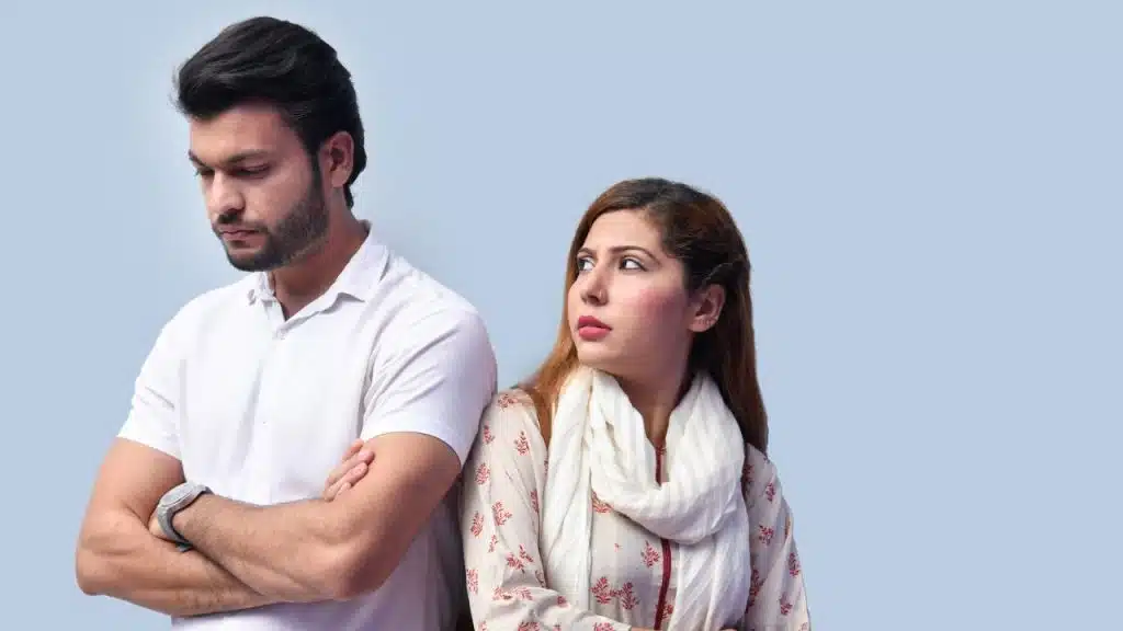 A man with crossed arms looks down while a woman looks back toward him.