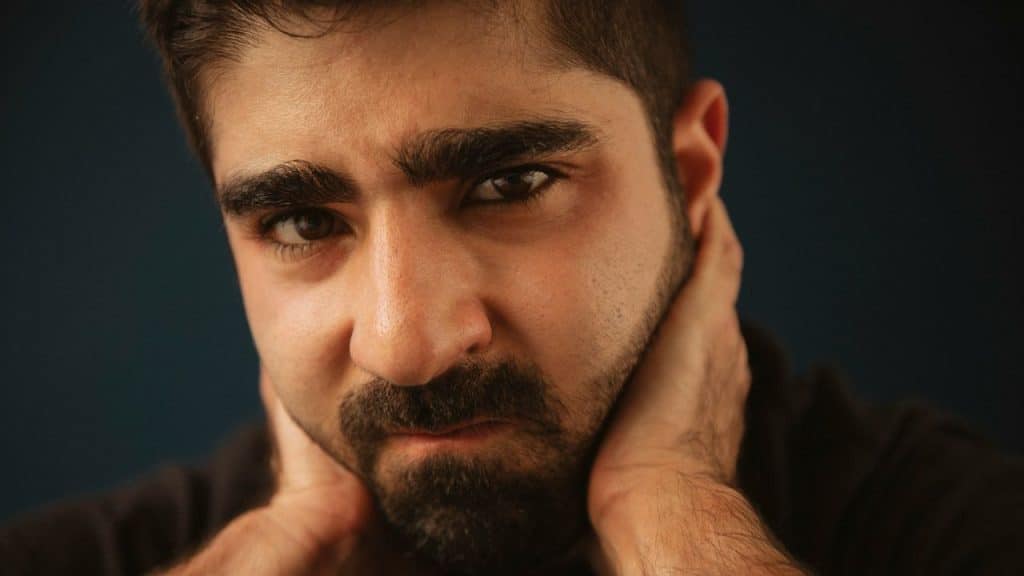 A close-up of a man with a beard and thick eyebrows, looking directly at the camera.