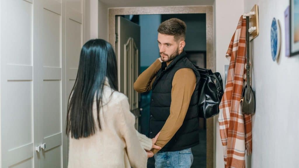 A man with a black bag stands in a doorway looking back at a woman.