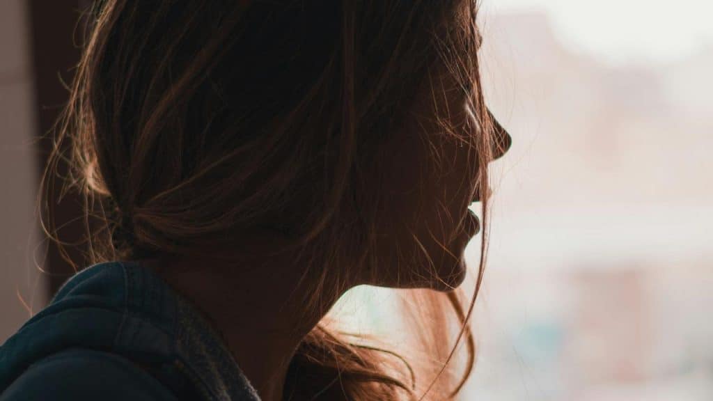 A side-profile silhouette of a person with loose hair lit by soft daylight.