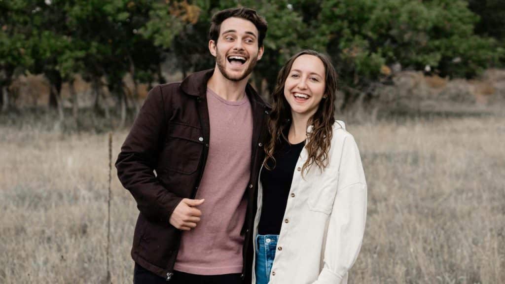 A happy couple standing outdoors in a field, smiling and laughing together.