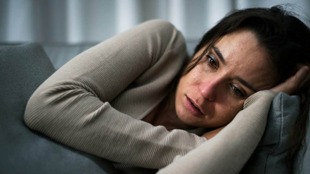 A woman with dark hair rests her head on her arms while lying on a sofa.