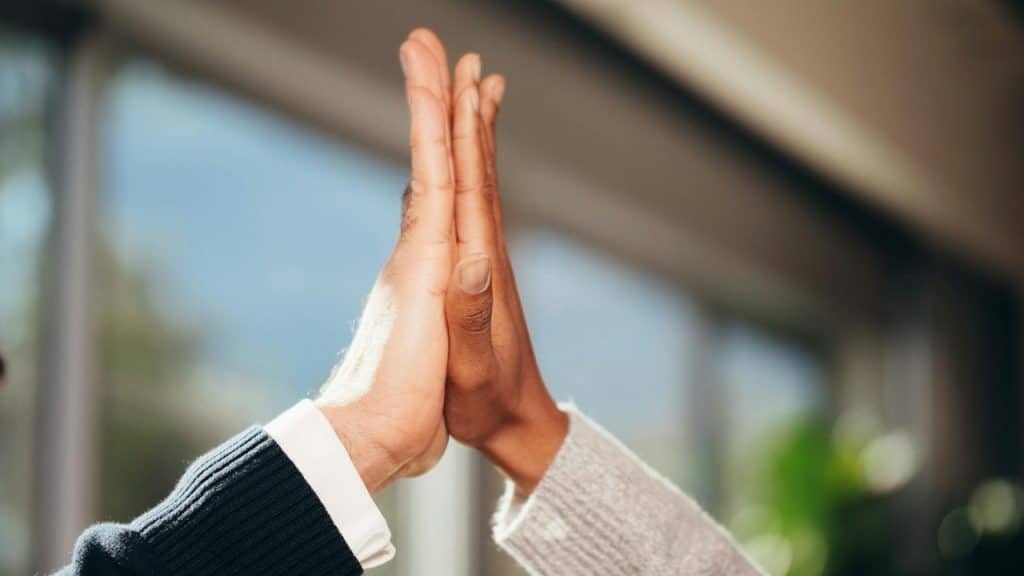 Two hands of different skin tones meet in the air to perform a high five.