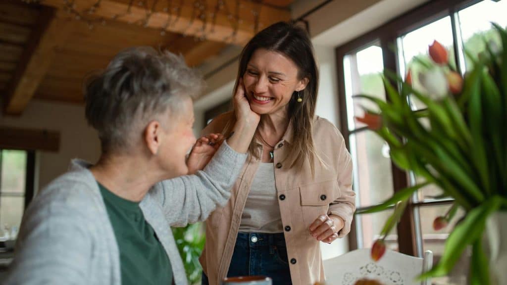 A person smiling warmly as another person touches their cheek in a cozy indoor setting.