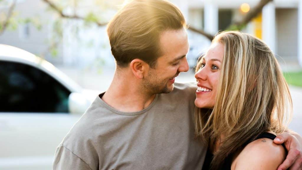 A happy couple smiling at each other in a close embrace outdoors on a sunny day.