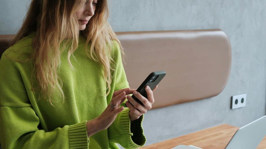 A woman in a green sweater using a smartphone at a table.