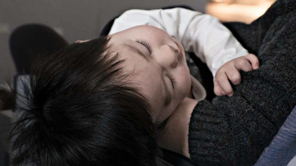A toddler asleep on an adult’s shoulder.