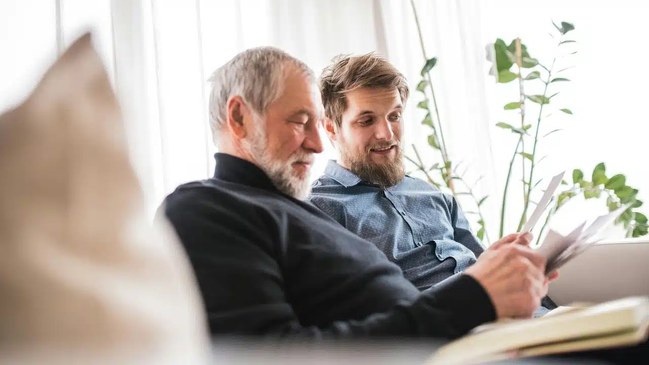A younger and older man sitting on a couch reviewing documents together.