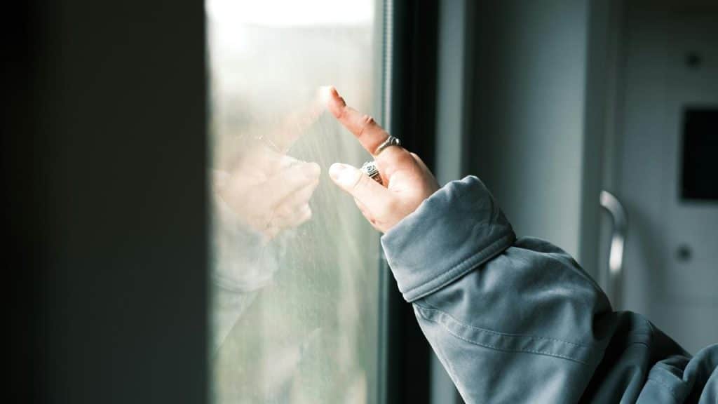 A hand with rings touching a window pane.
